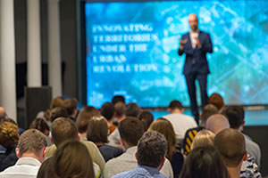 Photo from the audience's perspective looking forward towards the male lecturer who appears to be speaking on a stage